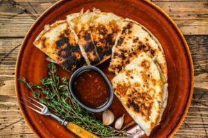 Mexican quesadilla with chicken, paprika, cheese and cilantro on wooden cutting board.
