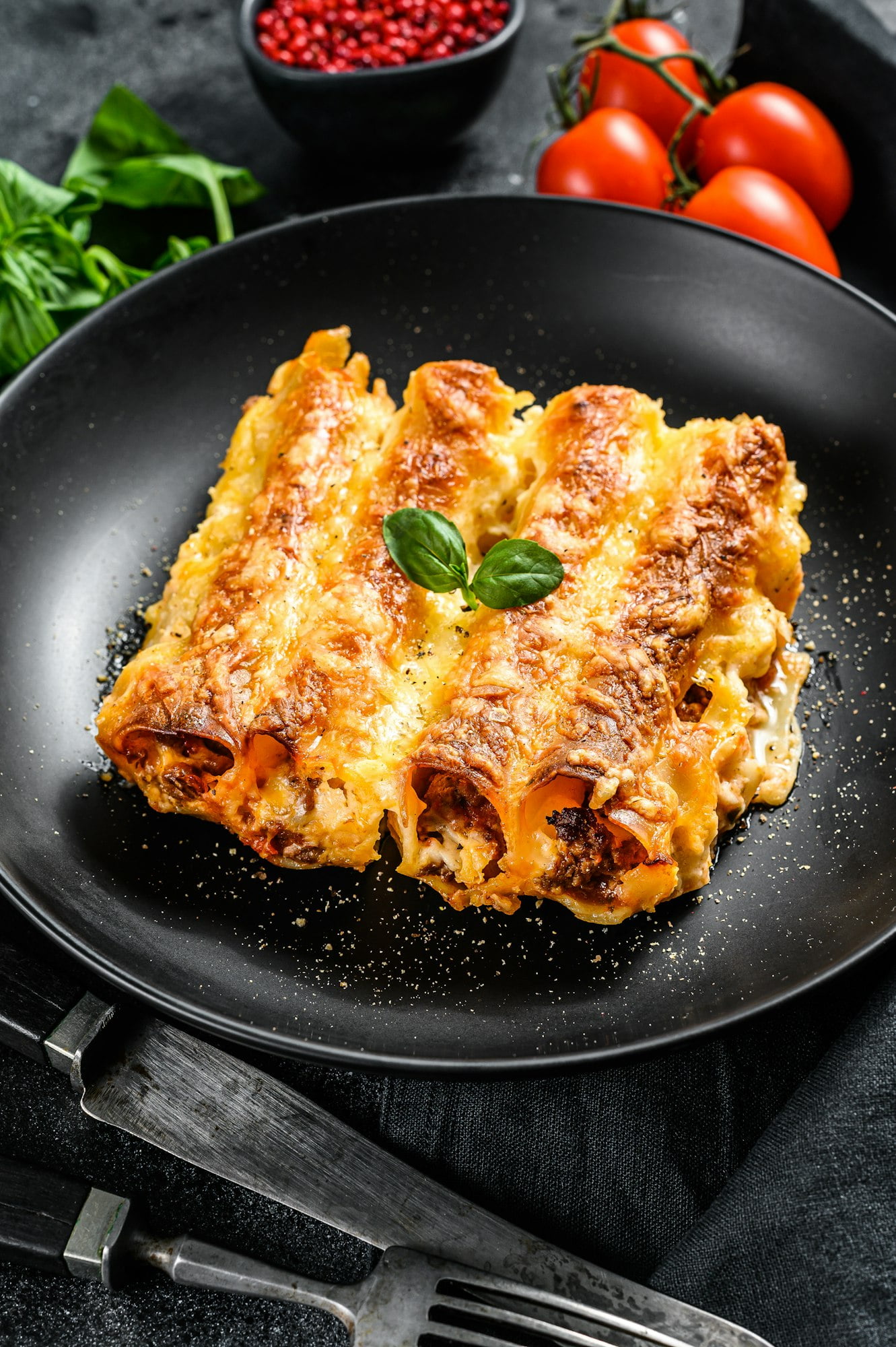 Italian homemade pasta cannelloni with beef and tomato sauce. Black background. top view