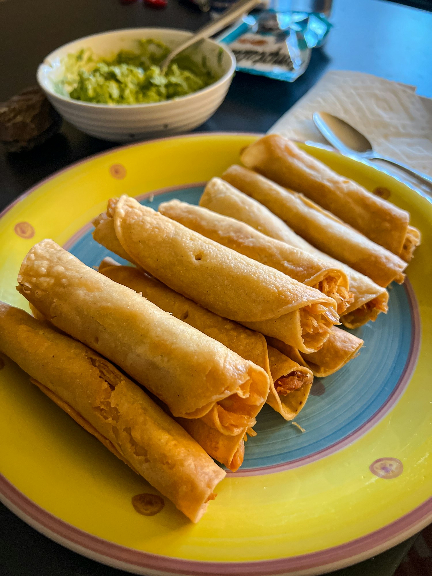 Mexican chicken Flautas taquitos on yellow plate with guacamole in the background for dinner.